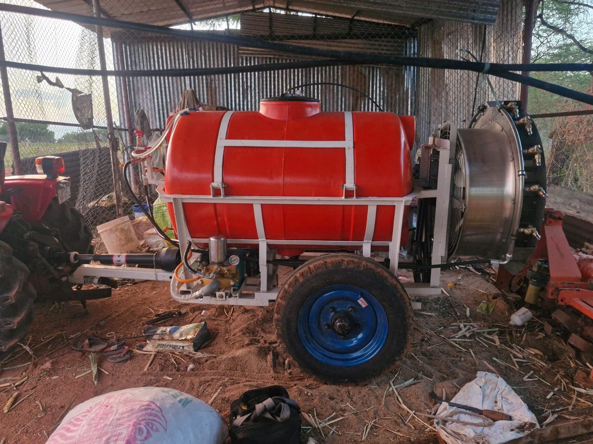 Red-tank air blast sprayer with white frame and steel fan housing, connected to a tractor PTO